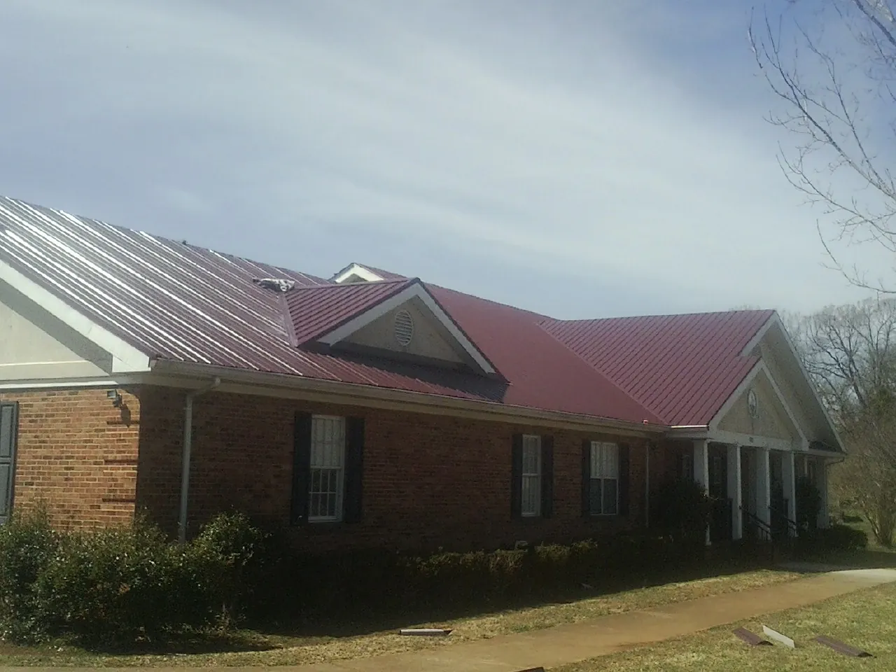 Red metal roof with gabled entries on a long brick building, from a Hail Damage Roof Repair job in Little Mountain