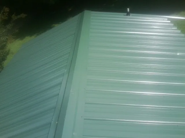 New green metal panels meeting at the ridge of a roof — Flat Roof Repair work by our crew in Little Mountain