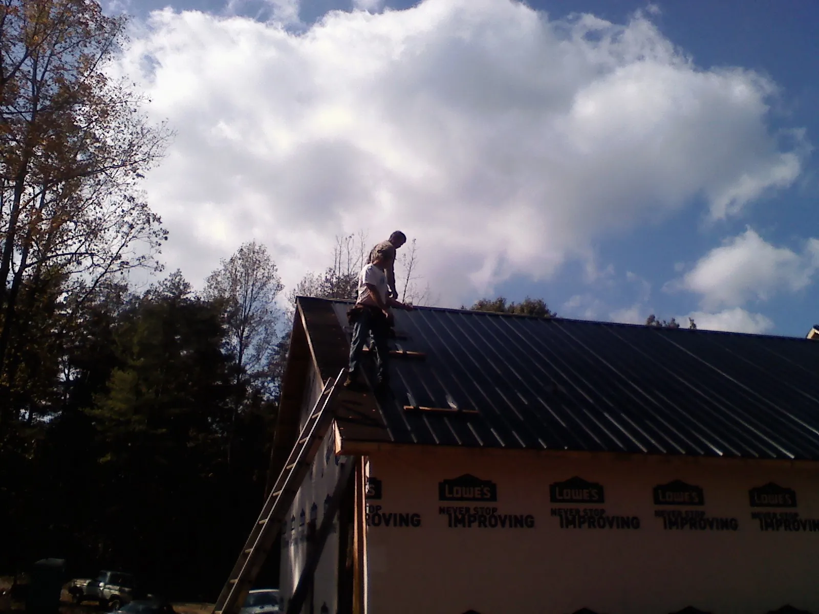 Roofer fastening dark metal panels high against a cloudy sky, from a Roof Inspection job in Little Mountain