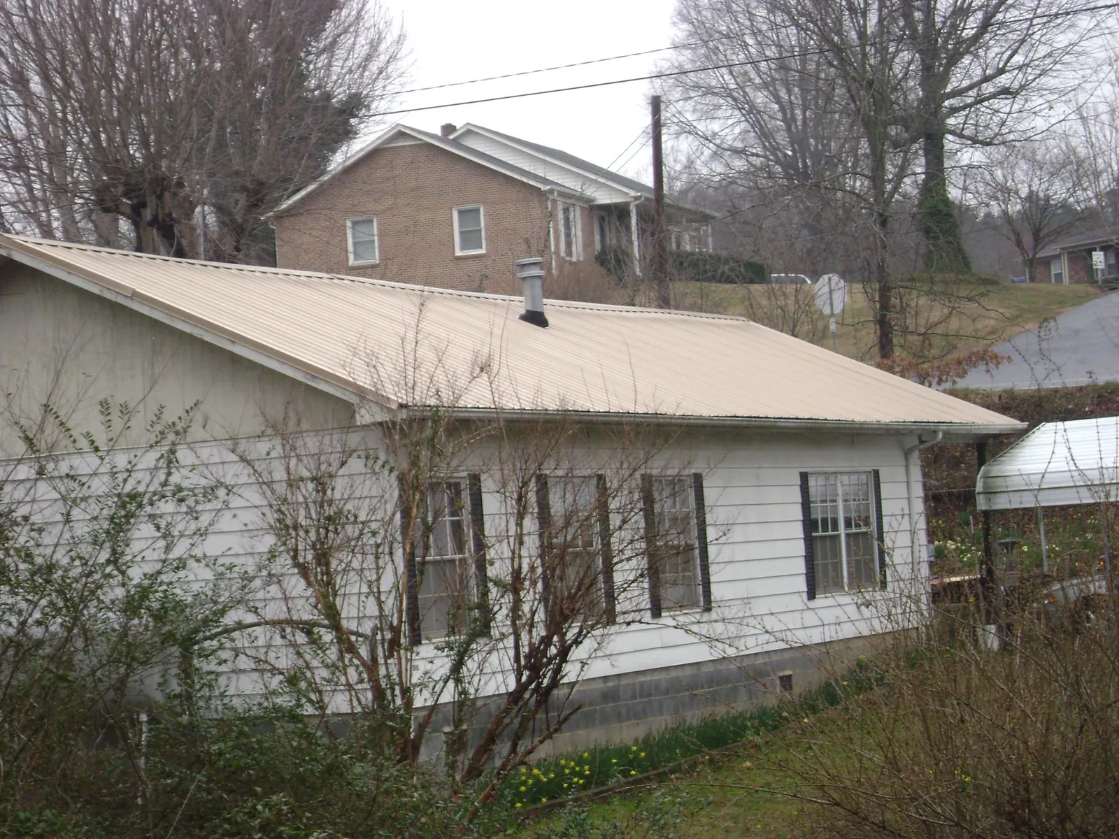 Tan metal roof on a white sided house set into a hillside — Commercial Roofing by Roofing Brothers in Little Mountain