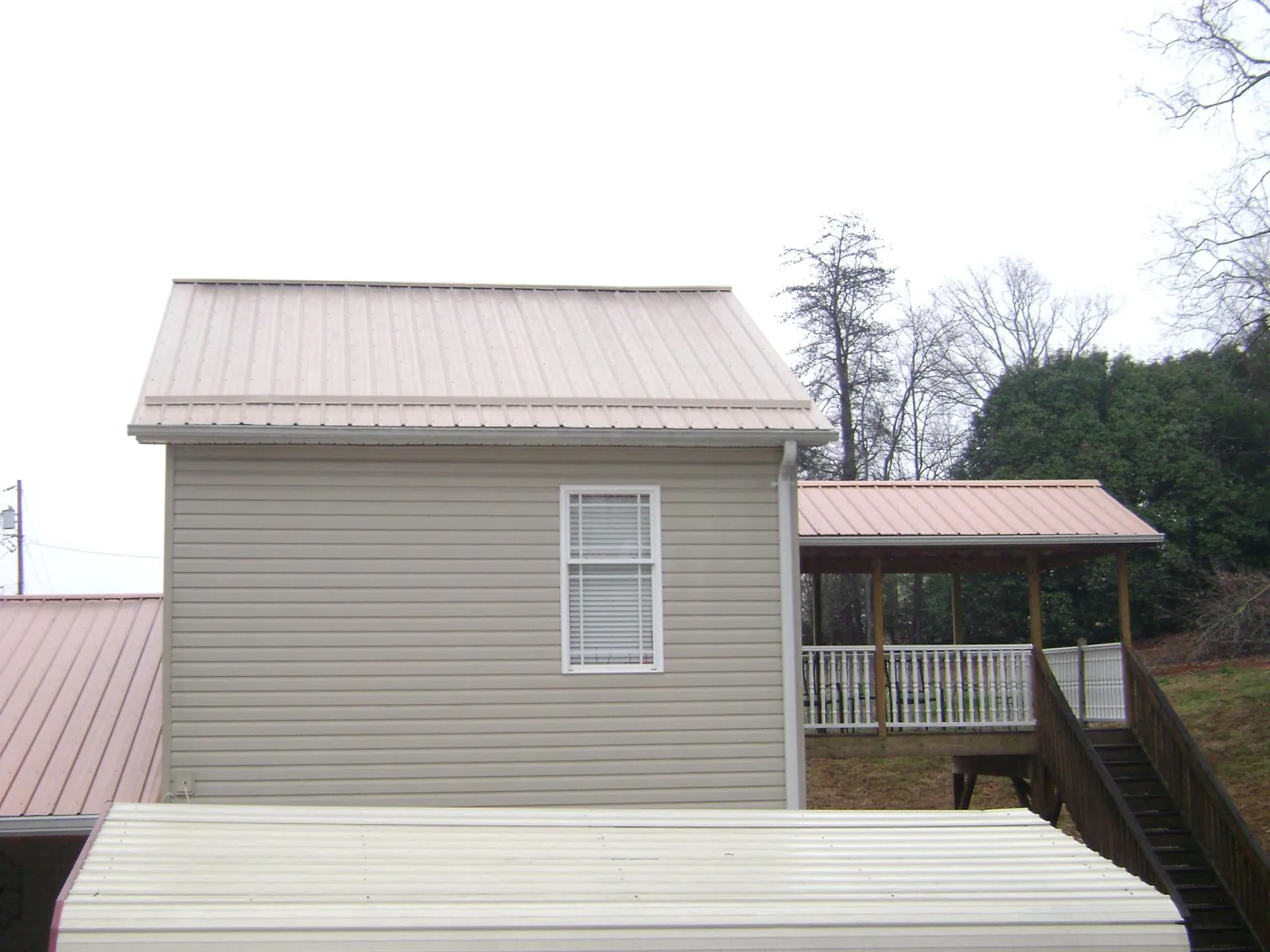 Tan metal roofs on a two story addition and attached porch, from a Roof Replacement job in Little Mountain